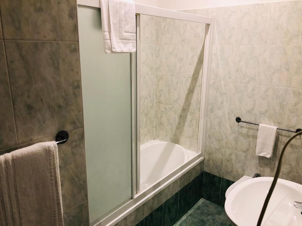Un baño con ducha de vidrio, lavamanos y un perchero para toallas.