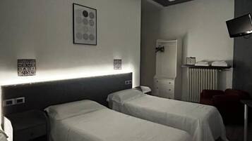 A hotel room with two single beds, a bedside table, a chair, a desk, and a television.