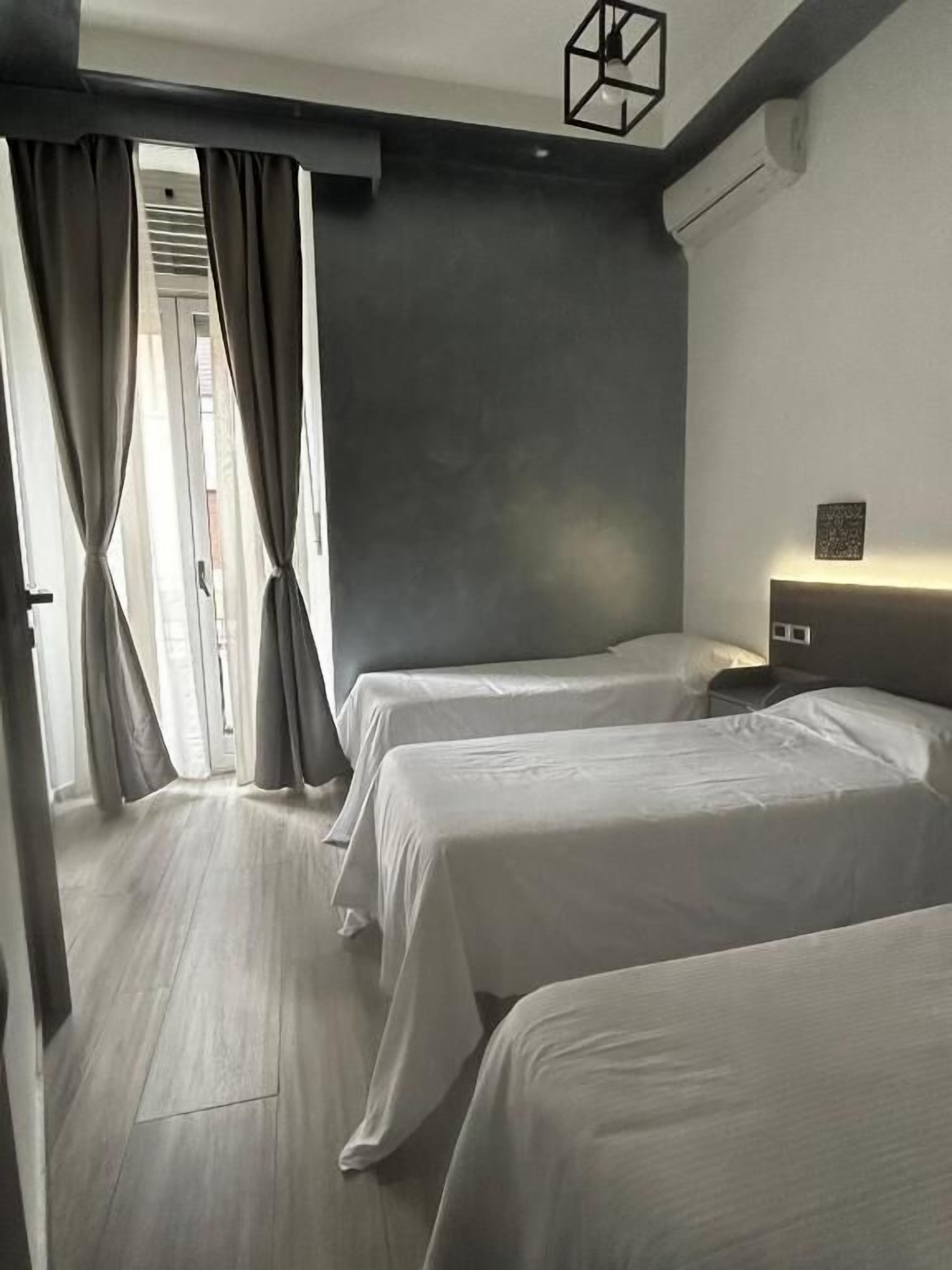 A hotel room with two beds, a bedside table, a lamp, and a view of the street through the window.