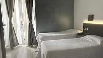 Une chambre d’hôtel avec deux lits, une table de chevet, une lampe et une vue sur la rue par la fenêtre.