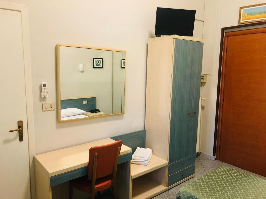 Een hotelkamer met een bureau, stoel, kledingkast en een bed.