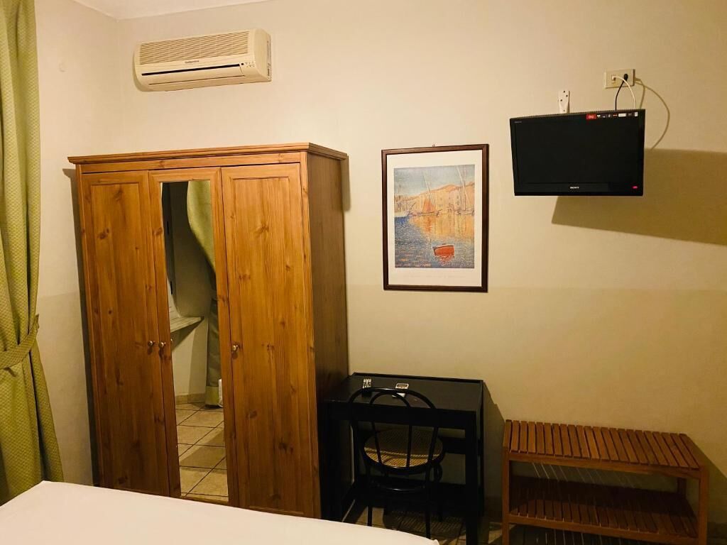 A hotel room with a wooden wardrobe, a desk with a chair, a television, and a framed picture on the wall.