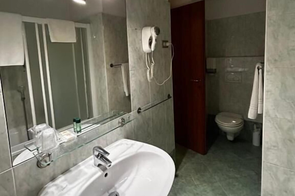 A bathroom with a white sink, a mirror, and a hairdryer on the wall.