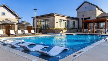 A swimming pool with lounge chairs and a building with large windows.