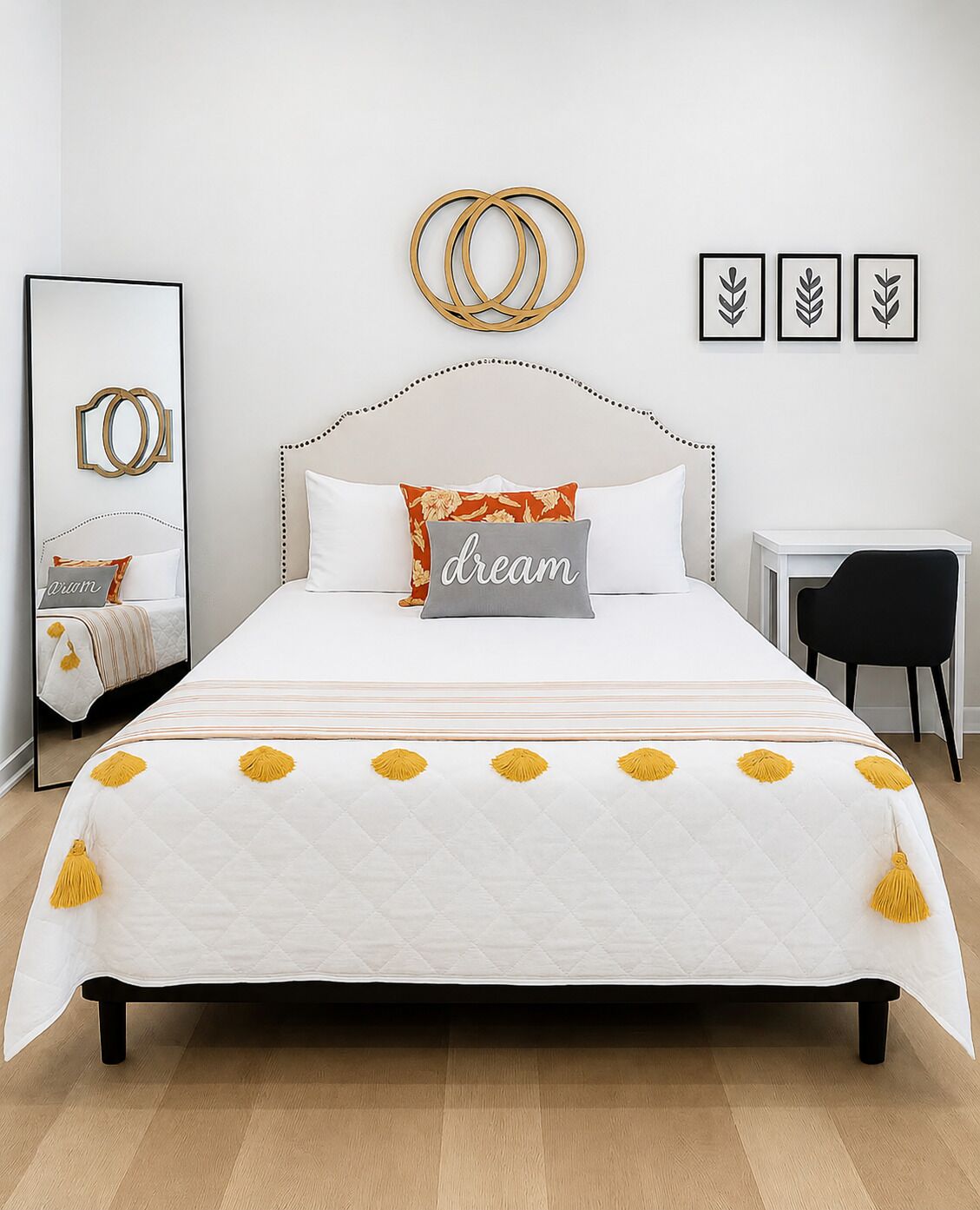 Una cama bien hecha con edredón blanco, almohadas decorativas y una colcha con flecos amarillos.