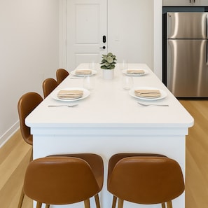 Une cuisine moderne avec un îlot central blanc, un réfrigérateur en acier inoxydable et des chaises en cuir marron.