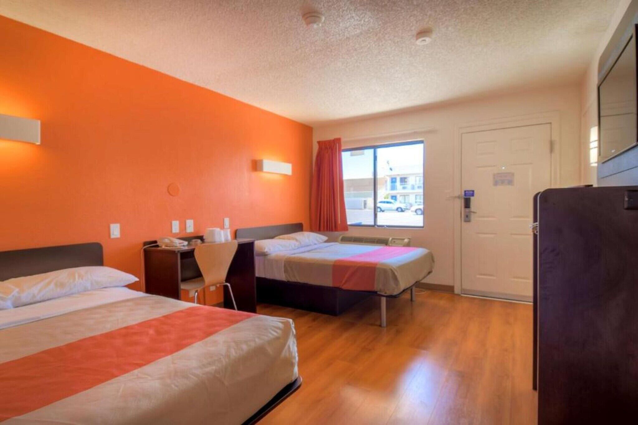 A hotel room with two beds, a desk, a chair, a window with a view of the street, and a door.