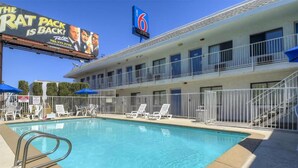 Un hôtel doté d’une piscine, de chaises longues et d’une enseigne annonçant un événement consacré au Rat Pack.