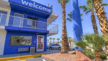 A blue building with a 'Welcome' sign, a balcony, and palm trees.