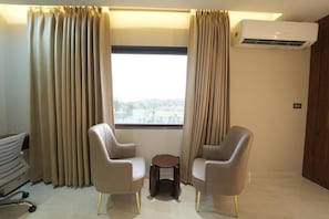 Una habitación con dos sillas, una mesita y un ventanal con cortinas.