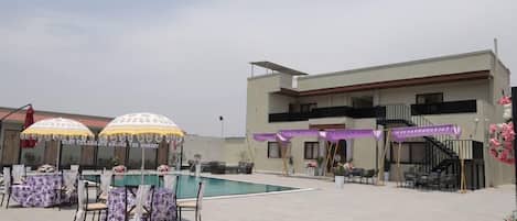 An outdoor pool area with tables and chairs, a building with a balcony, and a staircase.