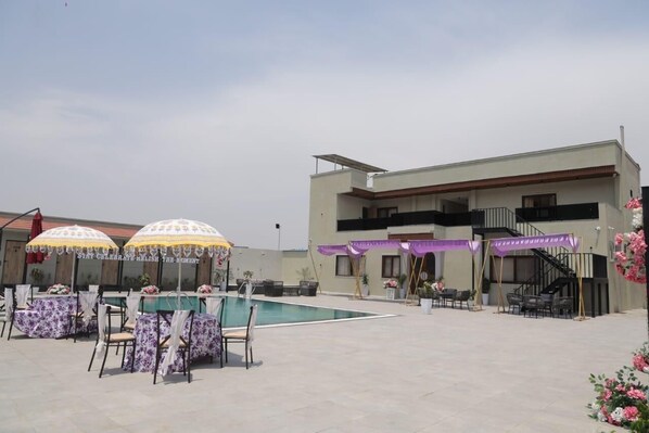 An outdoor pool area with tables and chairs, a building with a balcony, and a staircase.