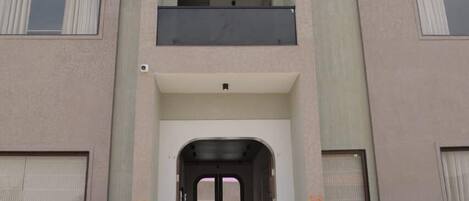 A multi-story building with a central entrance, balconies, and potted plants.