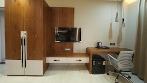 Habitación compacta con armario de madera, microondas integrado, una pequeña mesa de escritorio con silla y hervidor.