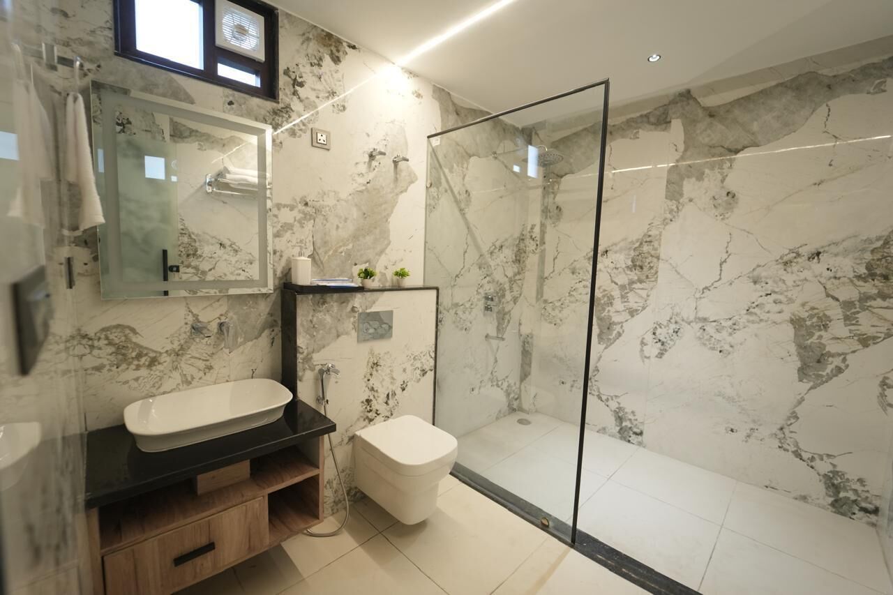 A modern bathroom with a glass-enclosed shower, a white sink, and a marble wall.