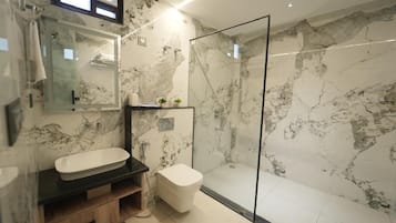 A modern bathroom with a glass-enclosed shower, a white sink, and a marble wall.