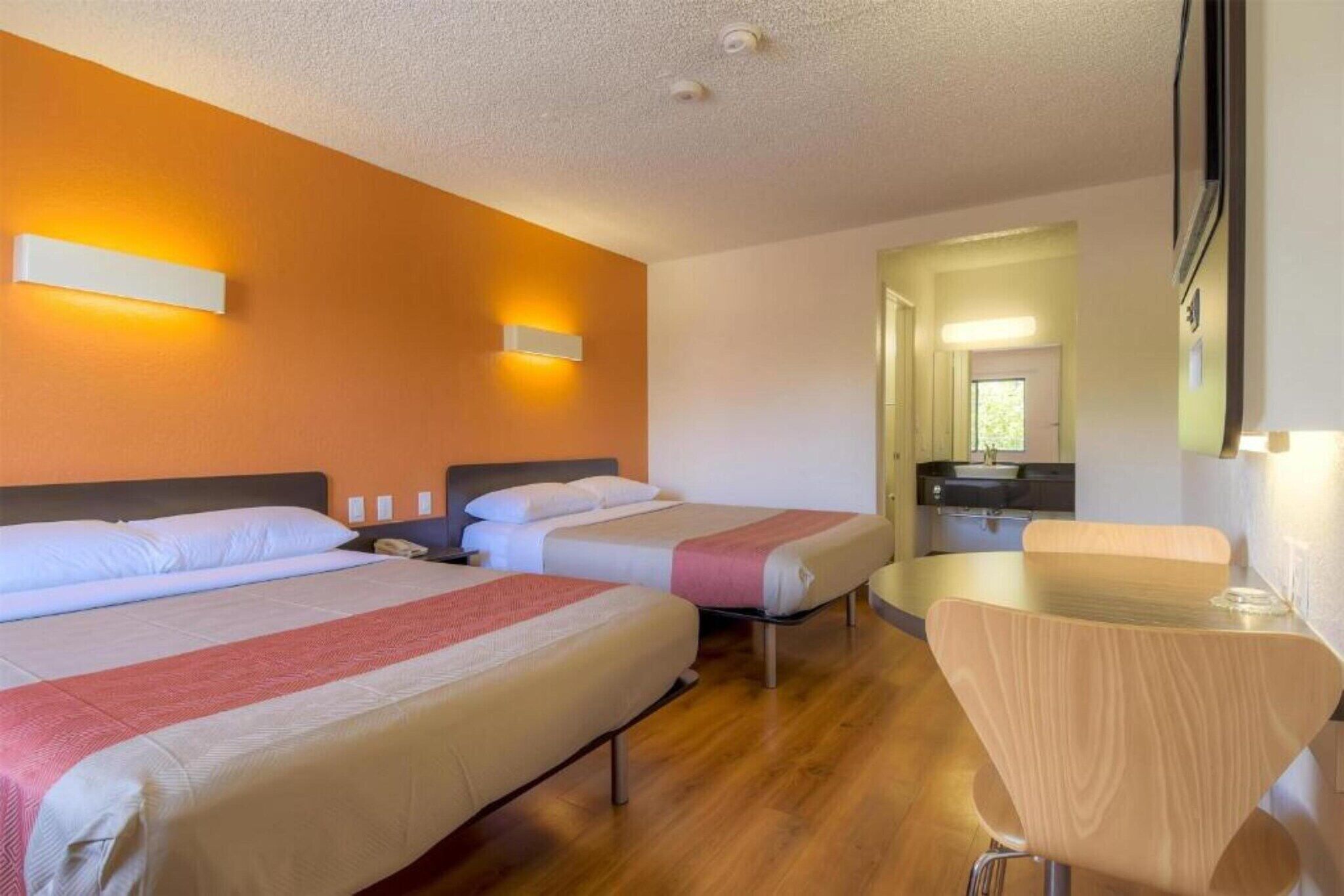 A hotel room with two beds, a small table, and a chair.