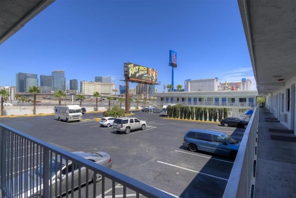 A parking lot with several cars, a billboard, and a city skyline in the background.