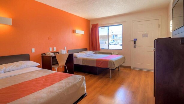 Hotelkamer met twee bedden, een bureau, een stoel, een raam met uitzicht op de straat en een deur.