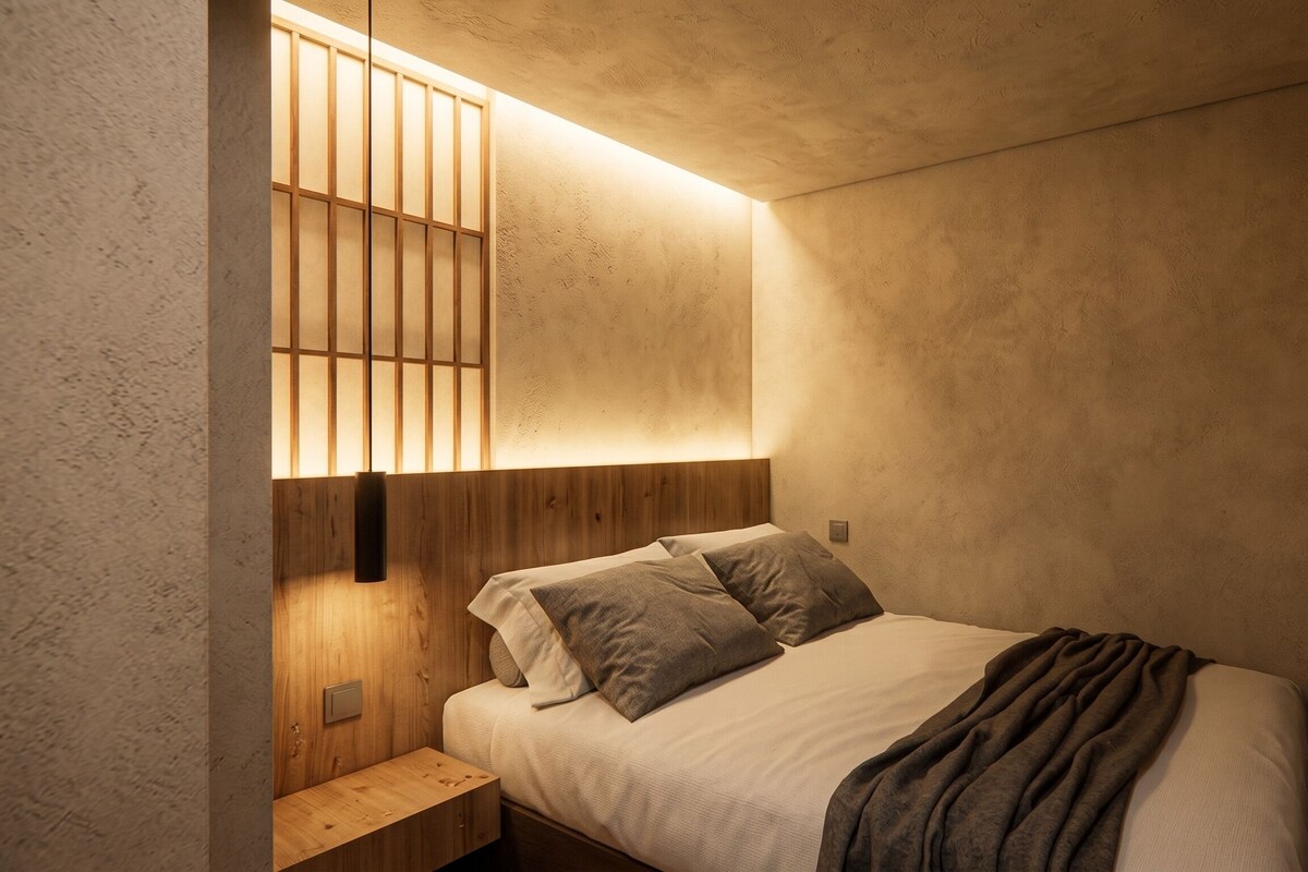 Una camera da letto con un letto, cuscini, un comodino e una lampada a parete.
