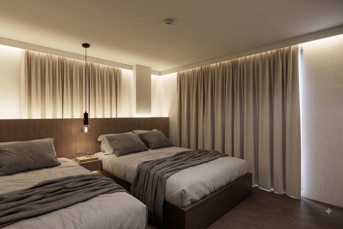 Camera d'albergo con due letti, un comodino, una lampada e un'ampia finestra con tende.