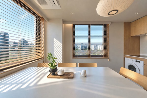 A modern kitchen with a built-in washing machine, a dining area with a table and chairs, and large windows with blinds. - The Gamro Gangnam (Seoul)