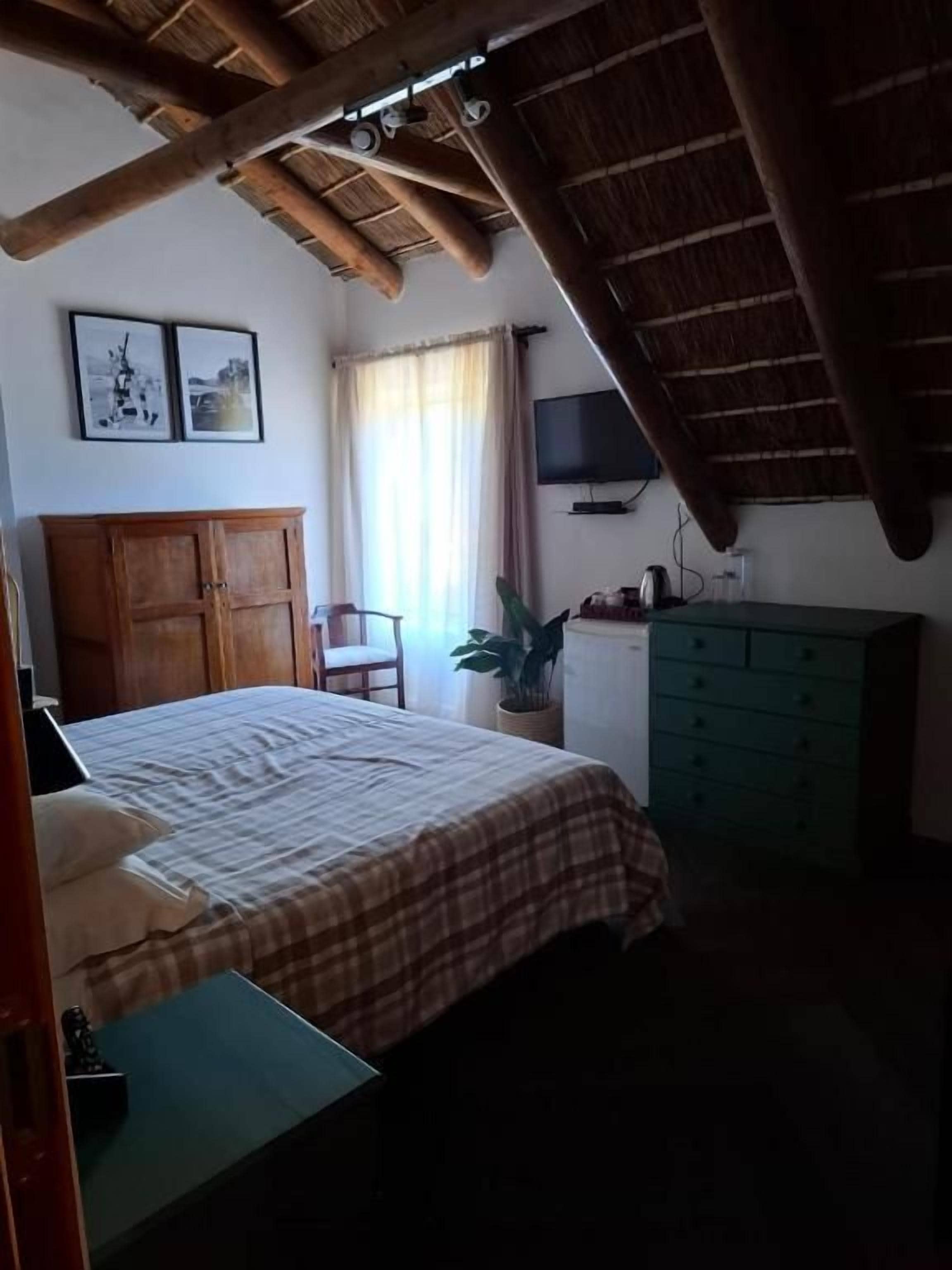 A bedroom with a bed, a wooden cabinet, a television, and a window with curtains.