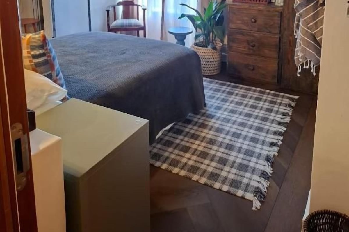 Un dormitorio con cama, cómoda, televisor y ventana con cortinas.