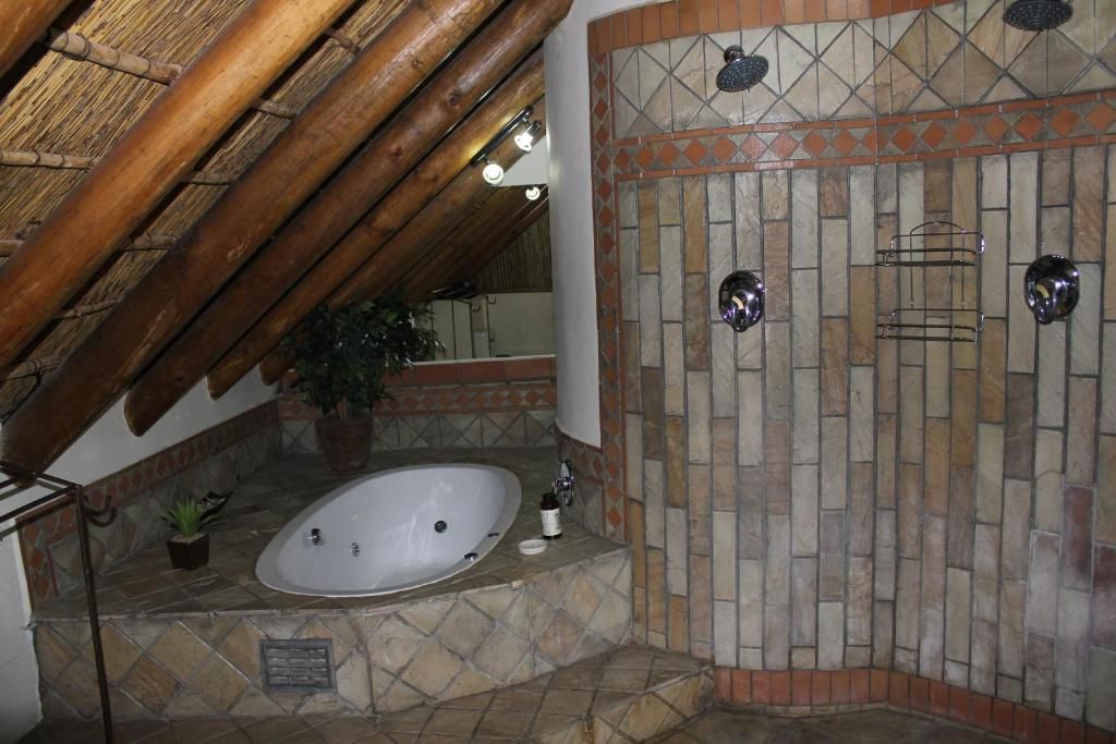 A bathroom with a stone-tiled shower wall, a bathtub, and a wooden ceiling.
