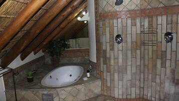 A bathroom with a stone-tiled shower wall, a bathtub, and a wooden ceiling.