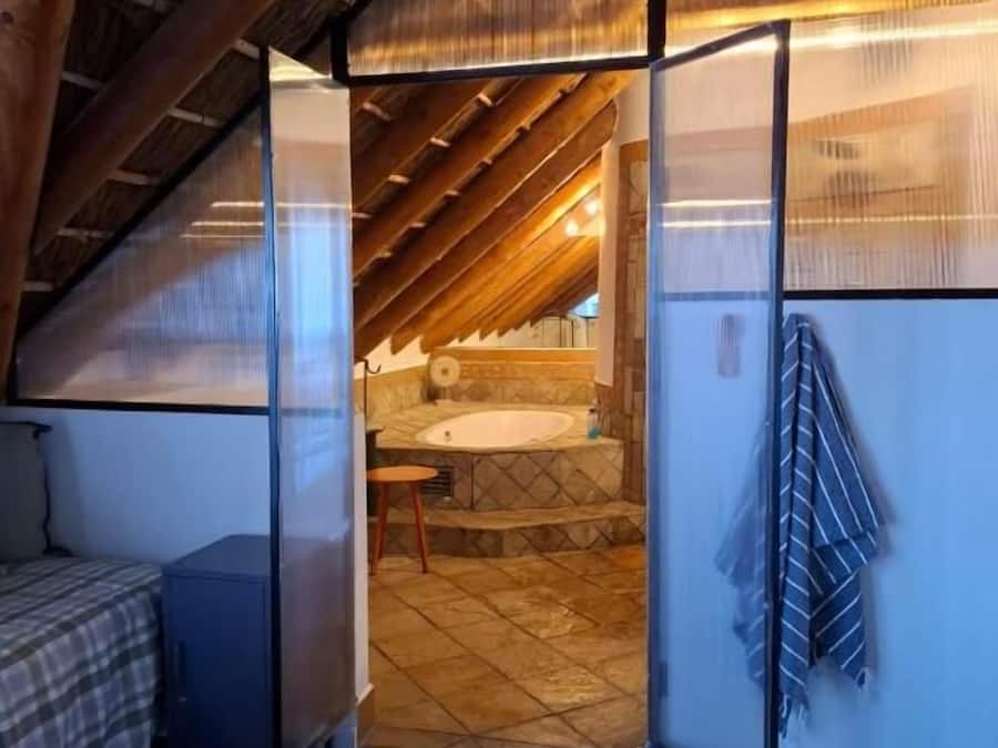 Un dormitorio con techo inclinado, una cama, una mesita pequeña y vistas a un baño con lavamanos y bañera.