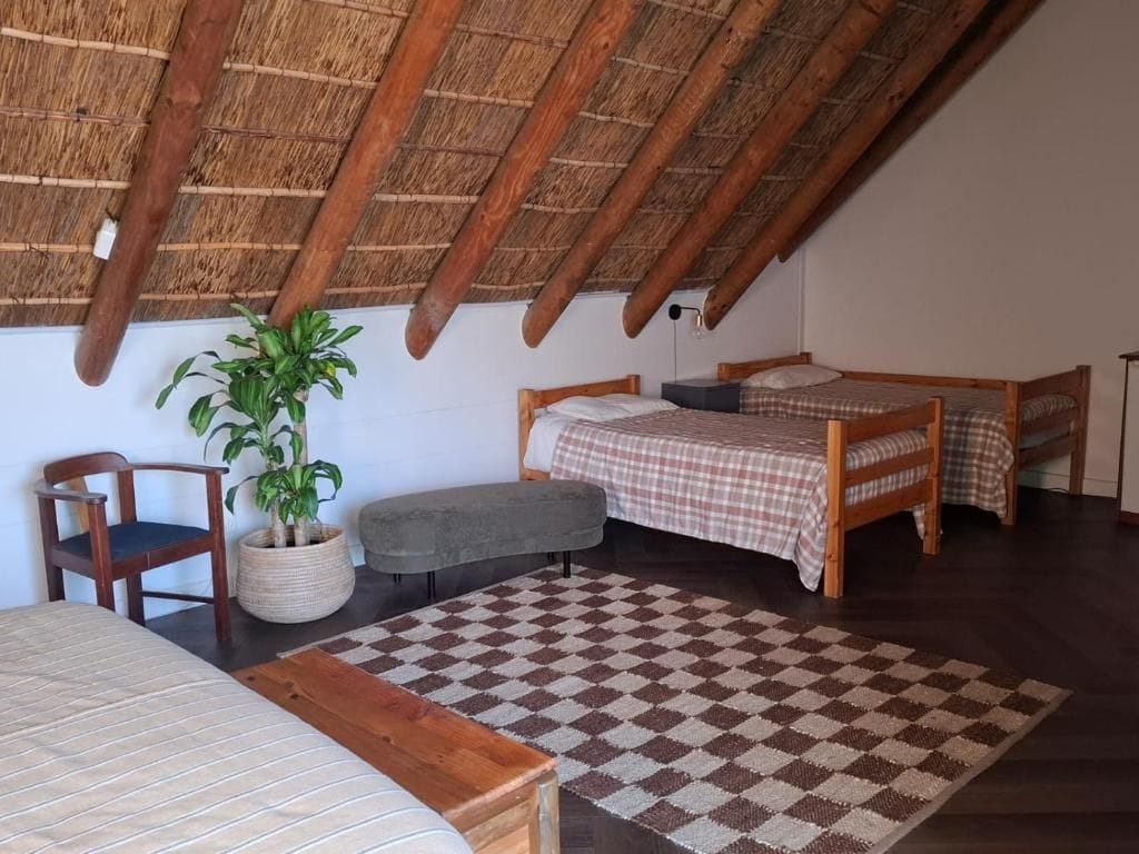 A room with a checkered floor, a bed, a chair, a small table, and a potted plant.