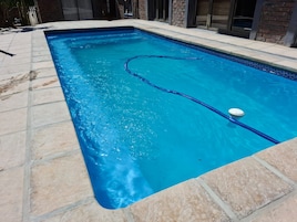 Piscina rectangular con agua cristalina azul, rodeada por un solárium con baldosas.