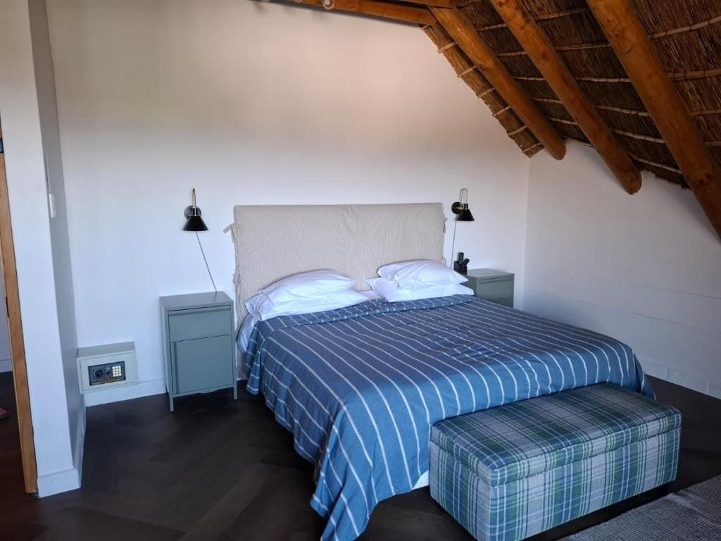 Un dormitorio con cama, mesitas de noche, un banco y techo inclinado.
