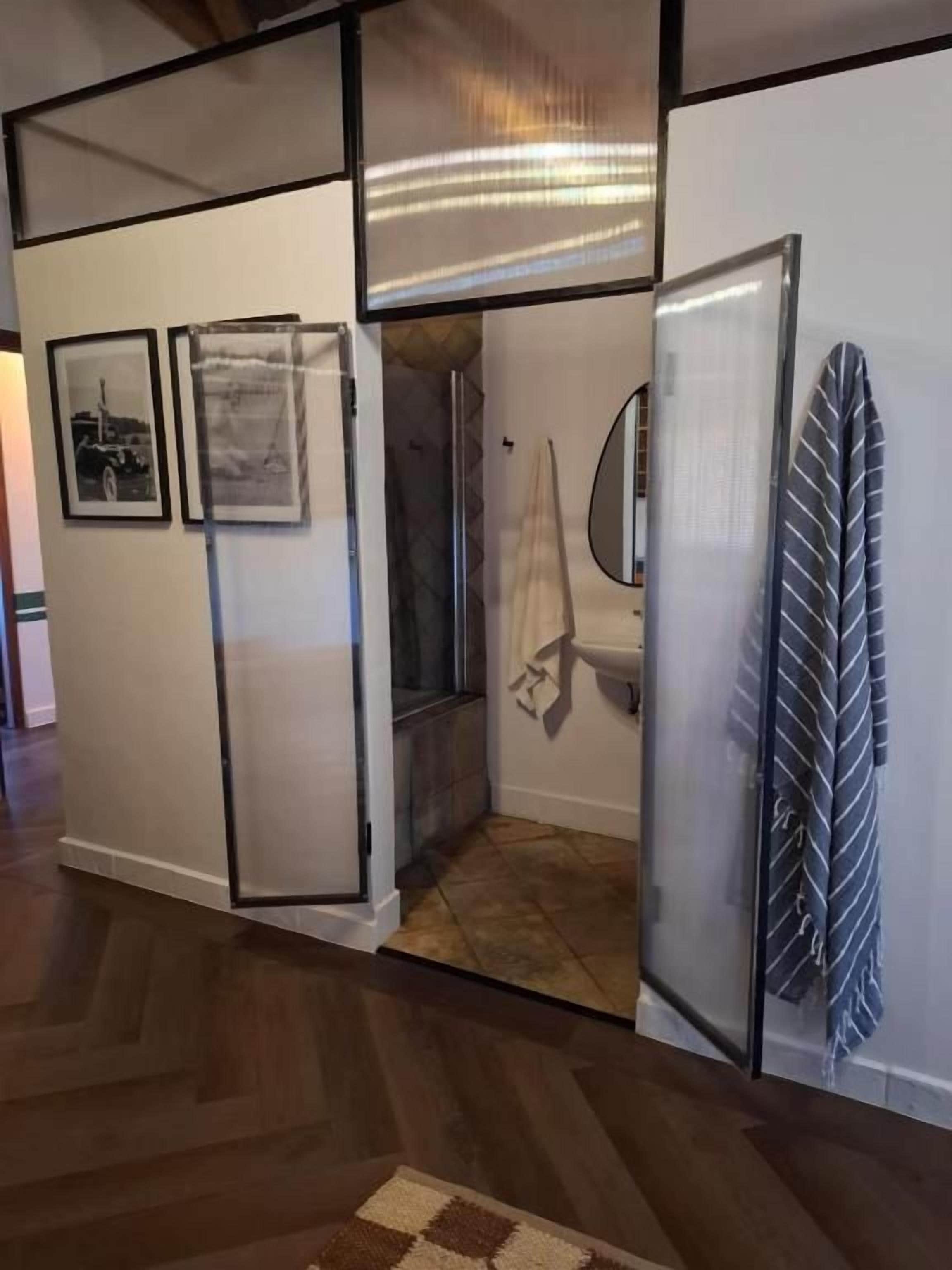 A room with a wooden floor, a glass partition, a shower area, and a towel hanging on the wall.