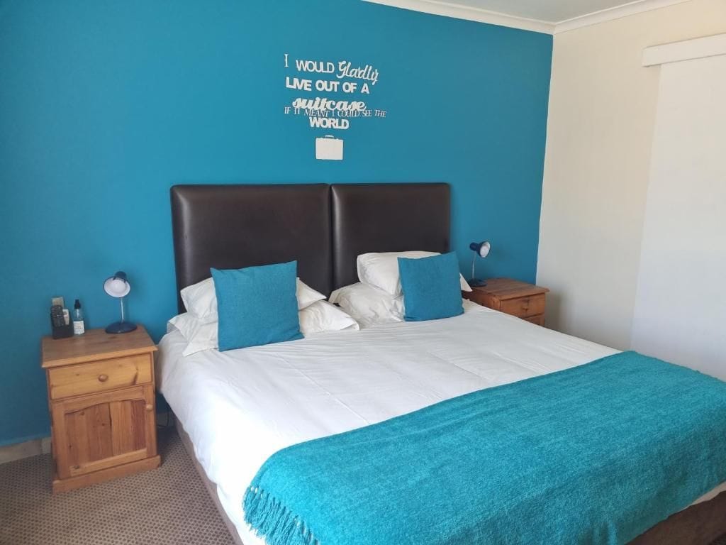 Ein Schlafzimmer mit einem Bett, einem Nachttisch, einer Wanduhr und einem motivierenden Zitat an der Wand.