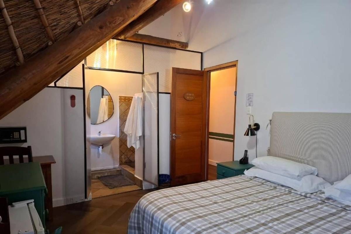 Un dormitorio con cama, mesita de noche, espejo, puerta y una pequeña mesa con una silla.