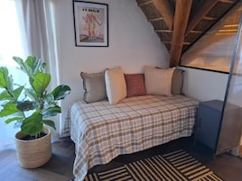 Un dormitorio con cama, una planta en maceta, un cuadro en la pared y techo de madera.