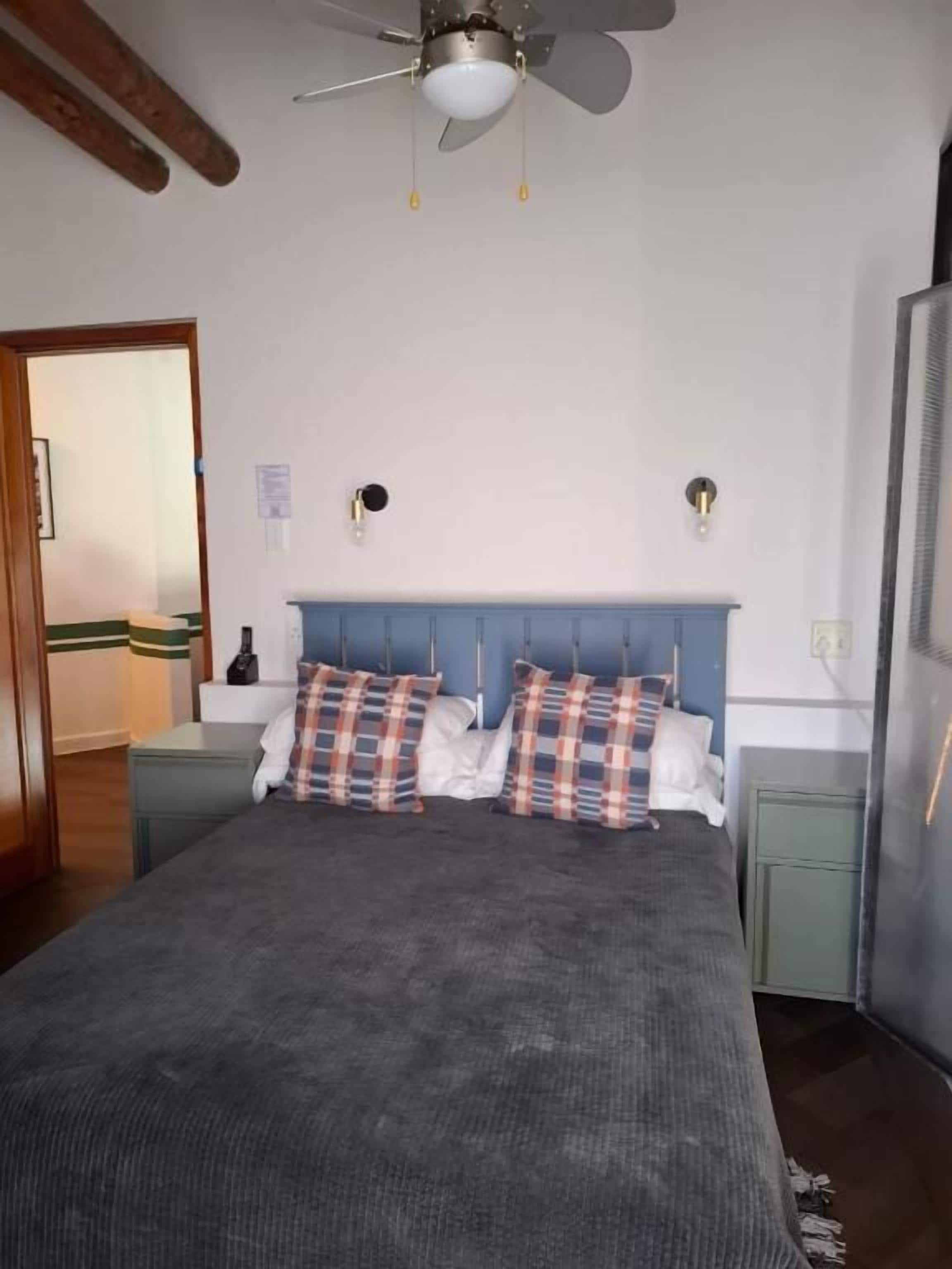 Een slaapkamer met een bed, een plafondventilator, een nachtkastje en een dressoir.