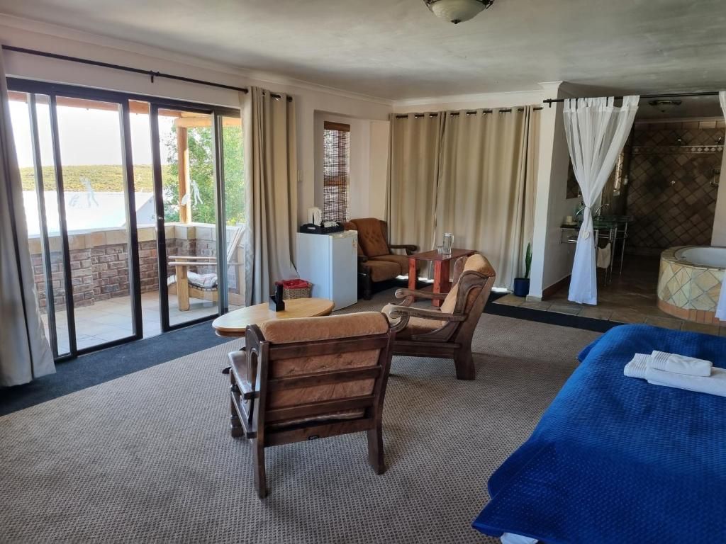 Een hotelkamer met een bed, twee fauteuils, een tafeltje en uitzicht op het omliggende landschap.