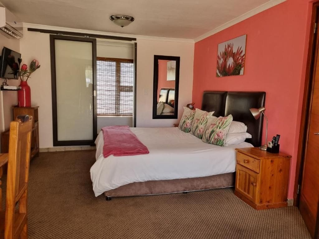 A bedroom with a bed, a nightstand, a wooden cabinet, a mirror, and a sliding glass door leading to a balcony.