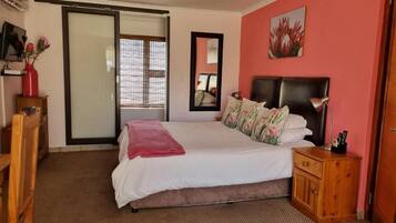A bedroom with a bed, a nightstand, a wooden cabinet, a mirror, and a sliding glass door leading to a balcony.