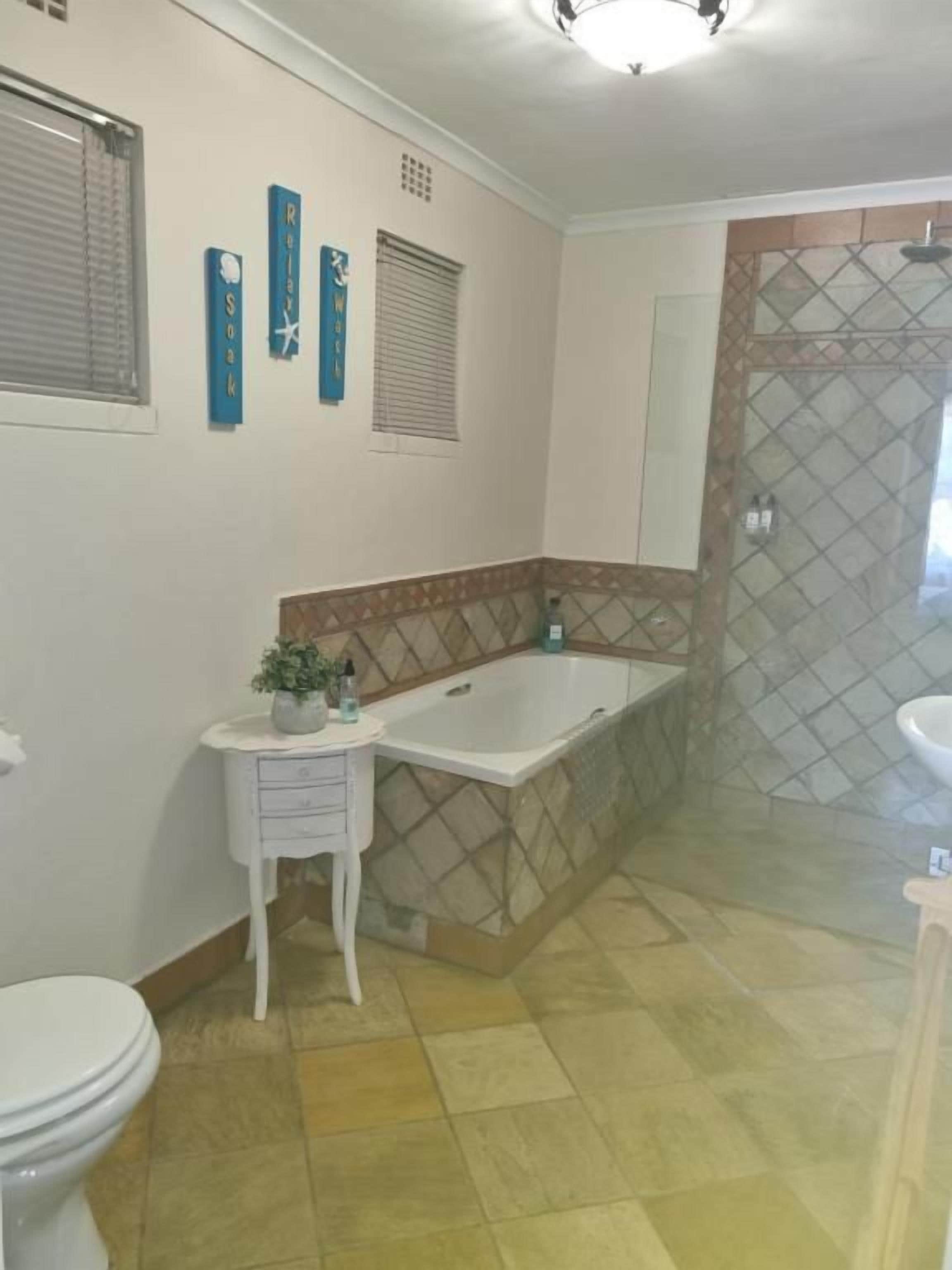 Un baño con bañera, inodoro y lavamanos. Hay azulejos decorativos en las paredes y una planta pequeña sobre una mesita.