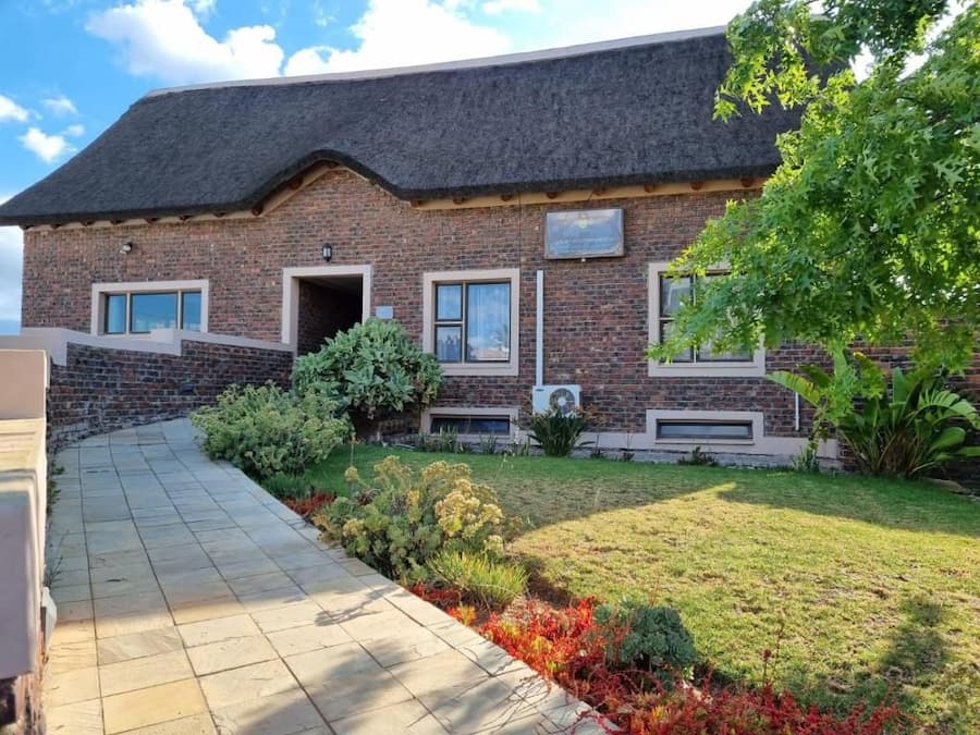 A brick building with a tiled pathway leading to the entrance, surrounded by well-maintained grass and shrubs.