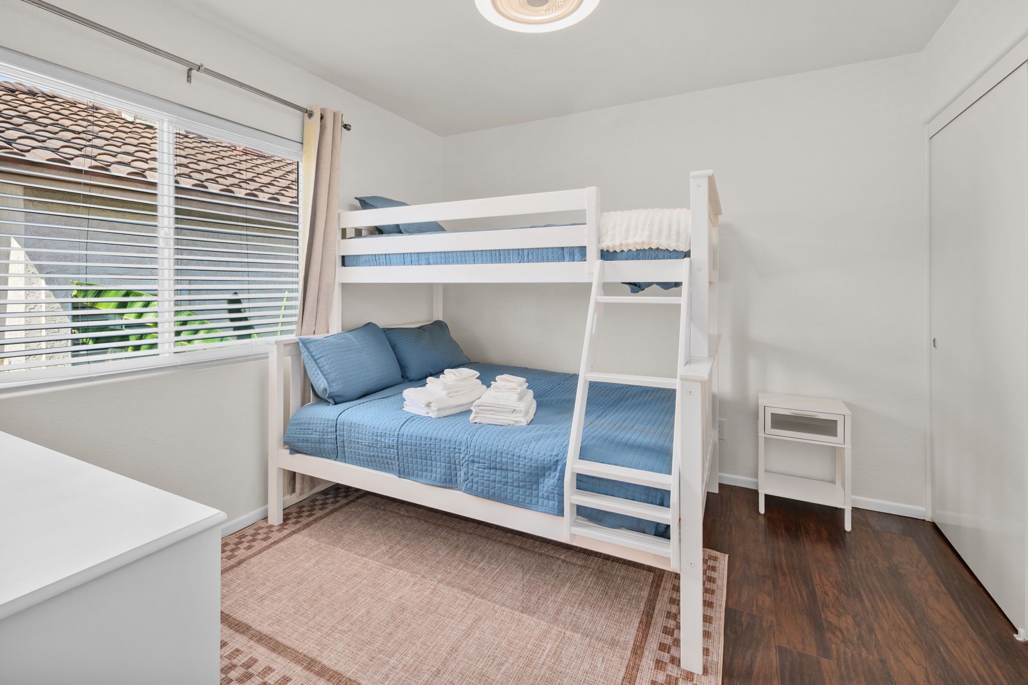 A bunk bed room with a desk and a small bedside table.