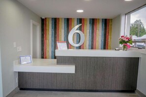 Un comptoir d’accueil orné d’un grand chiffre « 6 » sur le mur, un petit bureau sur lequel est posé un vase de fleurs et une fenêtre donnant sur des arbres.