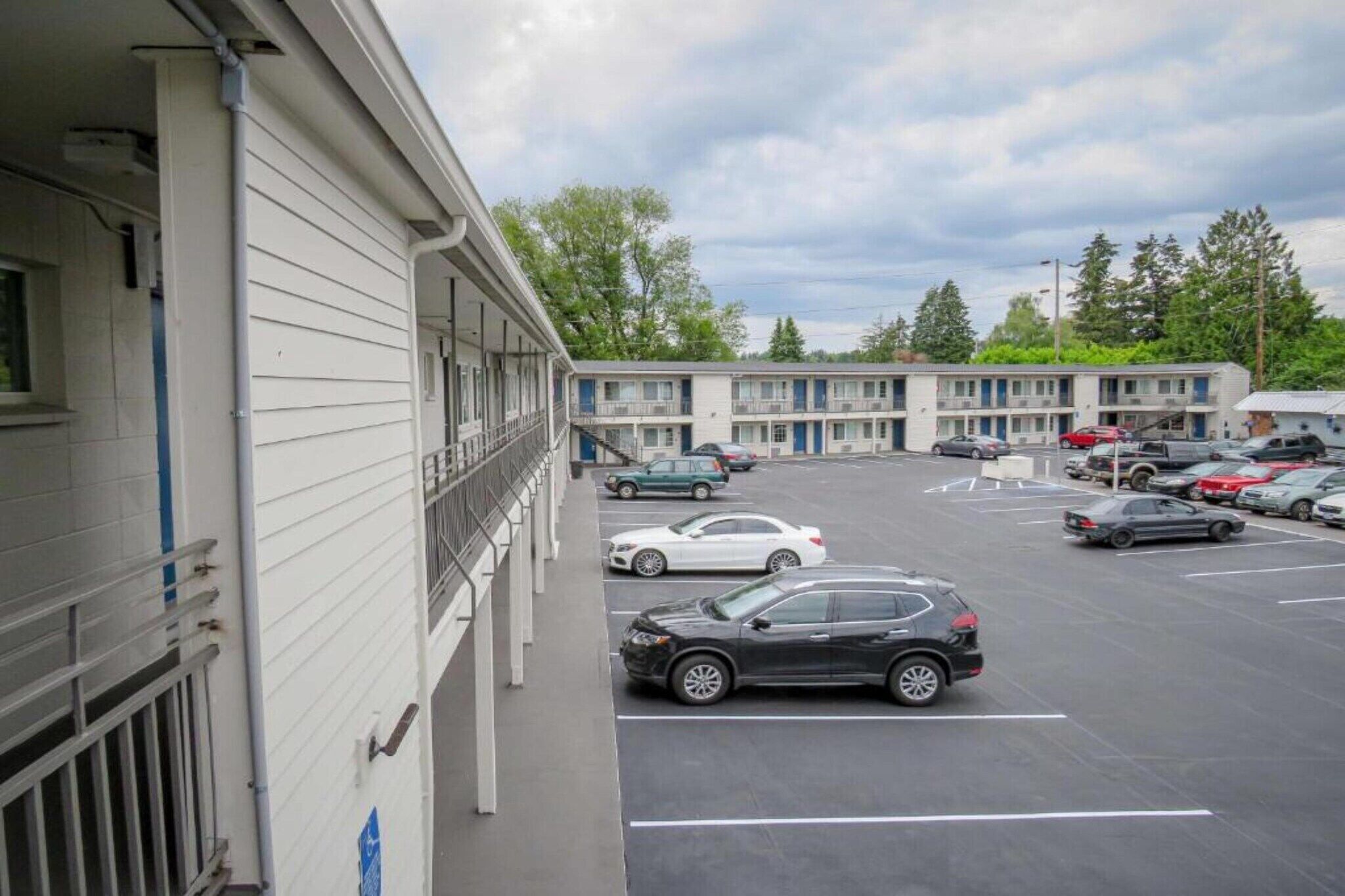 A motel with a parking lot, multiple cars parked, and a building with a balcony.