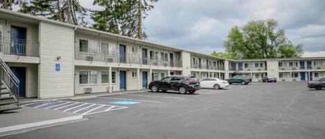 A motel with a parking lot, multiple units with balconies, and a clear sky.