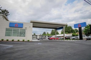 Un motel con un estacionamiento amplio, una zona de estacionamiento techada y un edificio con un letrero que dice '6'.