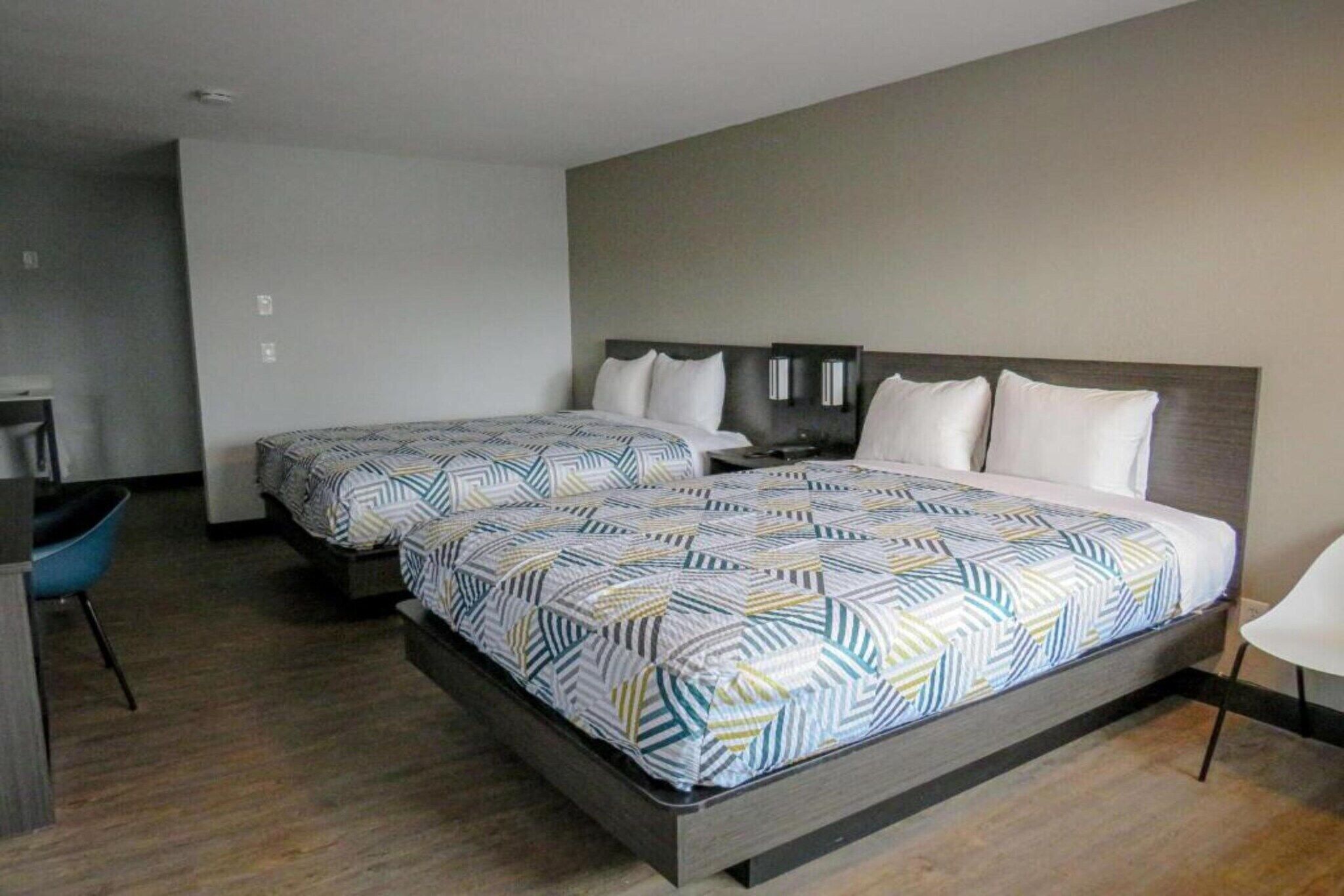 A hotel room with two beds, a desk, and a chair.
